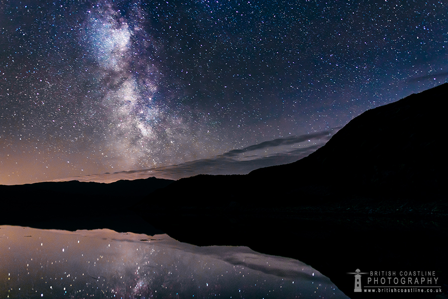 Milky Way, clear night sky, silhouetted sea cliffs, reflective sea loch