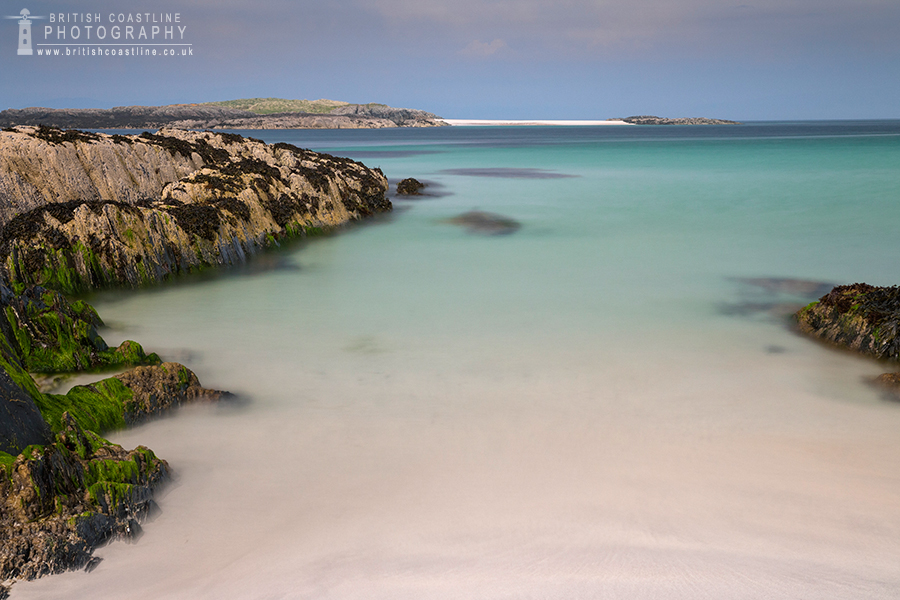 North Beach, Isle of Iona, smooth tropical sea framed either side with mossy rocks leading you towards an island with a beach