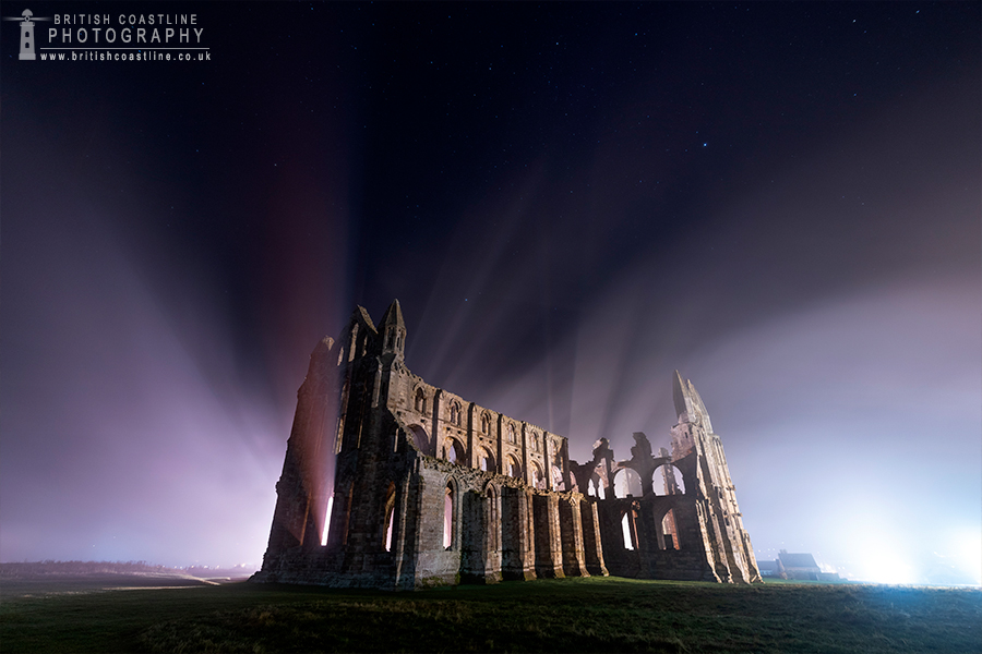floodlit whitby abbey with misty light rays shining through the open windows with the stars above